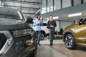 Portrait of male client talking to professional car dealer in dealership.