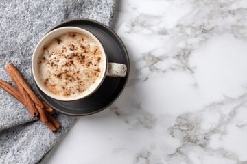 Cup of cappuccino with cinnamon on a marble table with a cozy blanket, perfect for a relaxing moment
