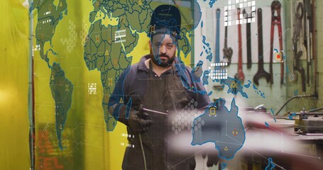 Welding Asian metalworker holding welding torch wearing apron at workshop, with digital map overlay