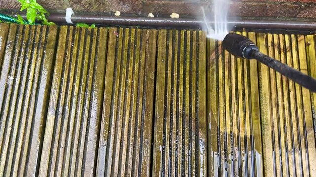 Pressure washing attachment being used to clean dirt and grime off the surface of wooden decking in the garden of a house. Before and after concept. No people.