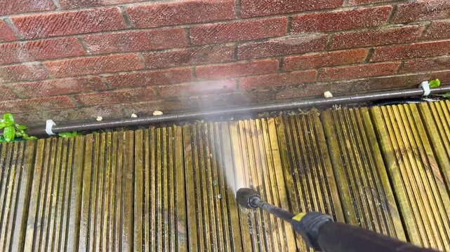 Pressure washing attachment being used to clean dirt and grime off the surface of wooden decking in the garden of a house. Before and after concept. No people.