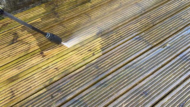 Pressure washing attachment being used to clean dirt and grime off the surface of wooden decking in the garden of a house. Before and after concept. No people.
