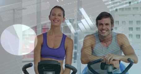 Pedaling smiling woman and man in sportswear on stationary bikes in gym, with translucent graphs