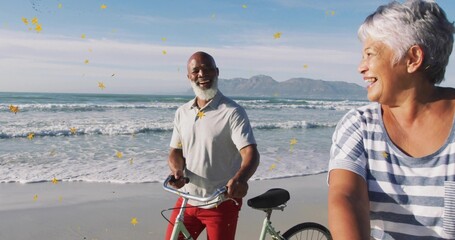 Smiling couple exchanging glances on sandy beach, holding two bicycles with floating confetti
