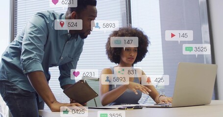 Collaborating colleagues in casual attire reviewing social analytics at desk, with laptop, tablet