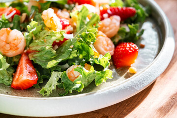 Gourmet salad with lettuce, strawberry, shrimps and walnuts on table in bright modern kitchen