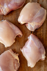 Raw Organic Boneless Skinless Chicken Thighs on a Wooden Board, top view.