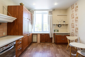 cozy kitchen with brown cabinets, a white-framed window, wooden floor, and neutral walls decorated with patterns