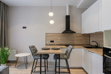 modern kitchen with white cabinets, a wooden backsplash, and a small dining area featuring two gray chairs, a wooden table set for two, and pendant lighting