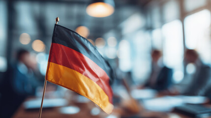 German flag on table in modern office setting with blurred business meeting in background, symbolizing diplomacy, politics, or international corporate cooperation.
