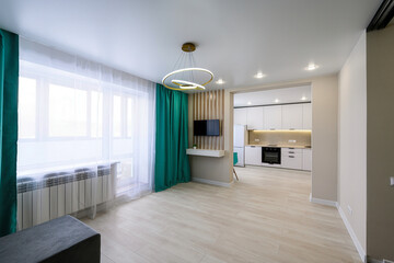 modern living room with a kitchen view, featuring a ring chandelier, green curtains, and a TV on a wall with wooden slats