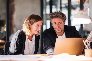 Two people collaborate on a laptop in a modern office