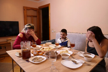 Mother and sister laughing at dinner while brother enjoys festive food.