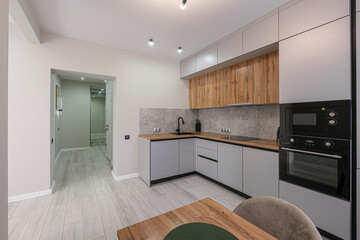 modern kitchen features gray cabinets, wood accents, and stainless steel appliances. The room is bright, with sleek design and a hallway visible in background