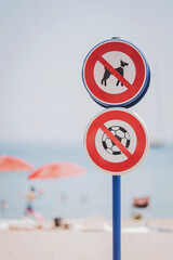 Beach safety signs reminding visitors to keep dogs and soccer balls off the sandy shore while enjoying a sunny day by the sea