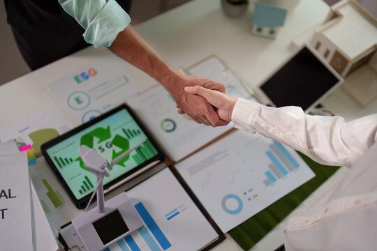 Top view of professionals shaking hands over ESG reports in a modern office.