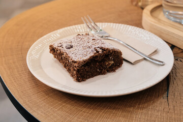 Close-up of chocolate brownie dusted with powdered sugar on a cozy wooden café table, highlighting texture and inviting dessert atmosphere.