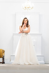 Fototapeta premium Bride in elegant white dress standing near vintage stove in mansion hallway