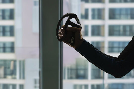 Silhouette of male arm doing exercise with expander to strengthen hand muscles. Man training grip strength with hand gripper in gym, bright window background