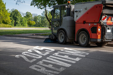 Street sweeper cleaning asphalt road with text 2025 REVIEW written on pavement. Symbolizing progress, city development and annual evaluation