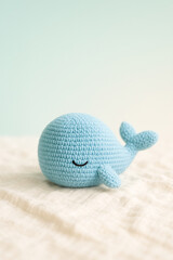 Close-up of a charming blue crochet whale toy resting on soft white fabric with a simple, pastel background, evoking a sense of craftsmanship, coziness, and playful charm.