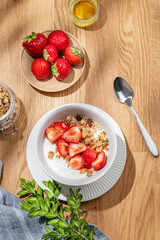 Granola or muesli with natural greek yogurt, strawberry and honey in a bowl on a wooden table with berries