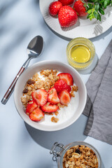 Granola or muesli with natural greek yogurt, strawberry and honey in a bowl on a blue background