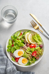 Tuna salad with cherry tomatoes, eggs, olives and cucumbers in a white plate on a light background
