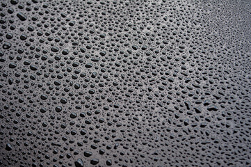 Closeup of black surface with dense water droplets forming textured condensation background.