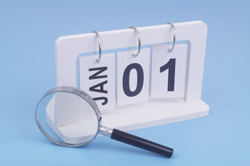 January, 1 on calendar under magnifying glass on blue background. Symbol of review of new year. 