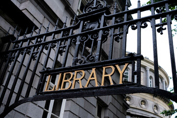 Fototapeta premium Elegant library entrance featuring ornate wrought iron gate with golden lettering amidst historic architecture
