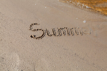 the inscription SUMMER on the sand on the river bank