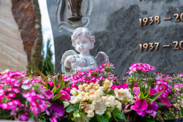 Kleiner Engel vor einem Grabstein inmitten von schönen Blumen auf einem Friedhof in Würzburg
