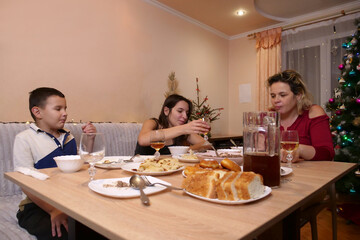 Family celebrating together, woman with children having dinner near festive Christmas tree.