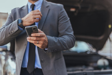 Business Professional Checking Smartphone Near Vehicle with Open Hood on Street