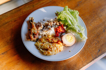 A mouth-watering plate of Nasi Campur, a traditional Indonesian mixed rice dish with chicken, egg, and vegetables on a wooden table