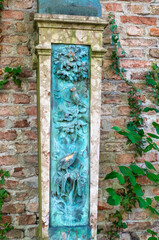 sehr alter Grabstein vor einer Ziegelmauer mit einer Einlage aus Metall mit Patina Alter Südfriedhof München