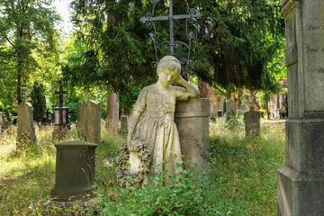 Grabsteine inmitten von Bäumen und Unkraut im Vordergrund eine Mädchenstatue an einem Grabstein Alter Südfriedhof München