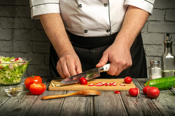 A skilled chef chops radishes and tomatoes on a wooden cutting board in a rustic kitchen. Fresh vegetables are displayed nearby, creating a vibrant cooking atmosphere