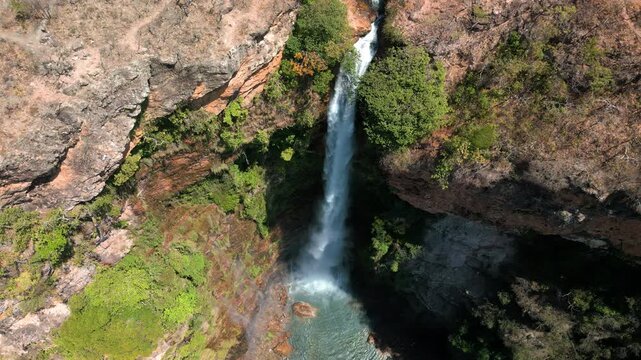 A vista a&eacute;rea revela uma cachoeira imponente que corta um c&acirc;nion de rochas avermelhadas, o fluxo intenso de &aacute;gua forma uma cortina branca at&eacute; desaguar em uma piscina natural abaixo.