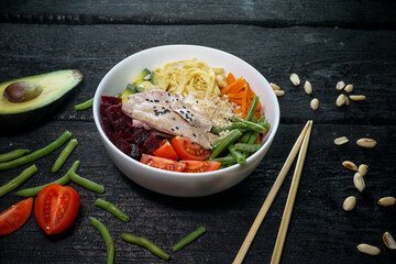 bibimbap with meat in a white plate on a dark background with avocado and chopsticks