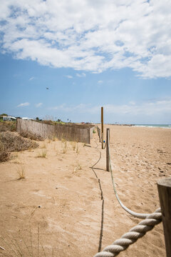 Bright, sunny day at a sandy beach with visible sea on the background. Fence runs across the beach, separating the main beach area from the slightly higher, vegetated dune area