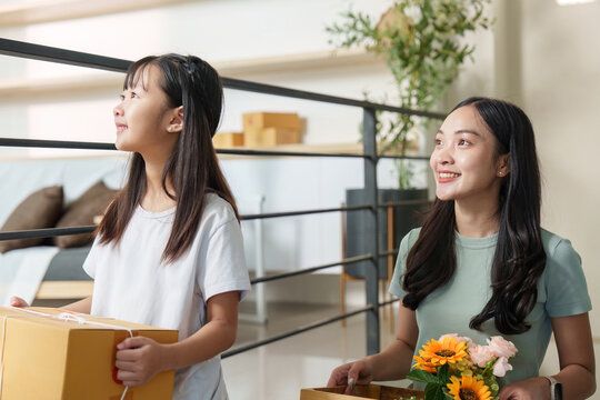 Family bonding. A mother and daughter carrying boxes and flowers, enjoying a joyful moment at home.