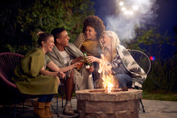 Lovely group of friends on autumn night sitting outdoors by the fire, enjoying time together.