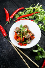 Fried meat with pepper and herbs on a white plate on a dark background
