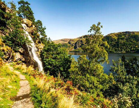 Scenic waterfall cascading down rocky cliff, tranquil lake and lush foliage - Powered by Adobe