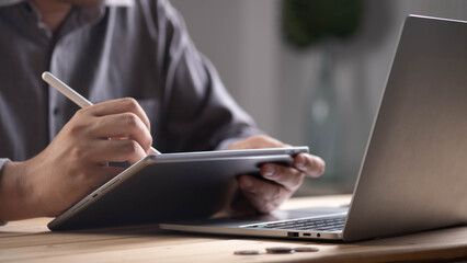 Close-up of businessman using digital tablet with stylus pen next to laptop, representing online work, digital creativity, remote office, technology innovation, and modern business productivity.