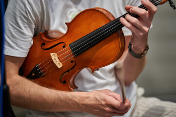 A musician in a casual t-shirt holds a violin in their hands, preparing for a performance, emphasizing the contrast between the modern attire and the classical instrument