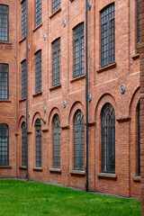 A close-up of an intricately designed brick building facade with arched windows, featuring metal outdoor stairs and black wrought iron lamps, showcasing the fusion of form and function in Łódź
