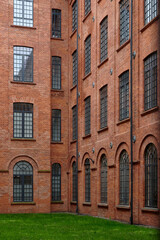 A close-up of an intricately designed brick building facade with arched windows, featuring metal outdoor stairs and black wrought iron lamps, showcasing the fusion of form and function in Łódź
